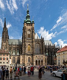 barevná fotografie katedrály svatého Víta při pohledu z jihu, nad katedrálou je modrá obloha s bílými oblaky, před katedrálou stojí množství turistů