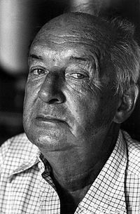 A photograph of Vladimir Nabokov. Wearing a collared shirt, Nabokov is pictured in his later years, with aging skin and white hair.