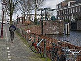 Amsterdam, old city - biking along the canal Nieuwe Herengracht with water lock and bridge Scharrebiersluis; free photo, Fons Heijnsbroek, 10 April 2022