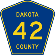 A blue pentagon with yellow text "42" inside, and small yellow text "DAKOTA COUNTY" surrounding the numeral