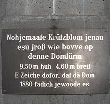 Inschriften auf Kölsch gehören zum Kölner Stadtbild.

Hochdeutsch: Nachgemachte Kreuzblume, genauso groß wie oben auf den Domtürmen, 9,50 m hoch 4,60 m breit. Ein Zeichen dafür, dass der Dom 1880 fertig geworden ist.