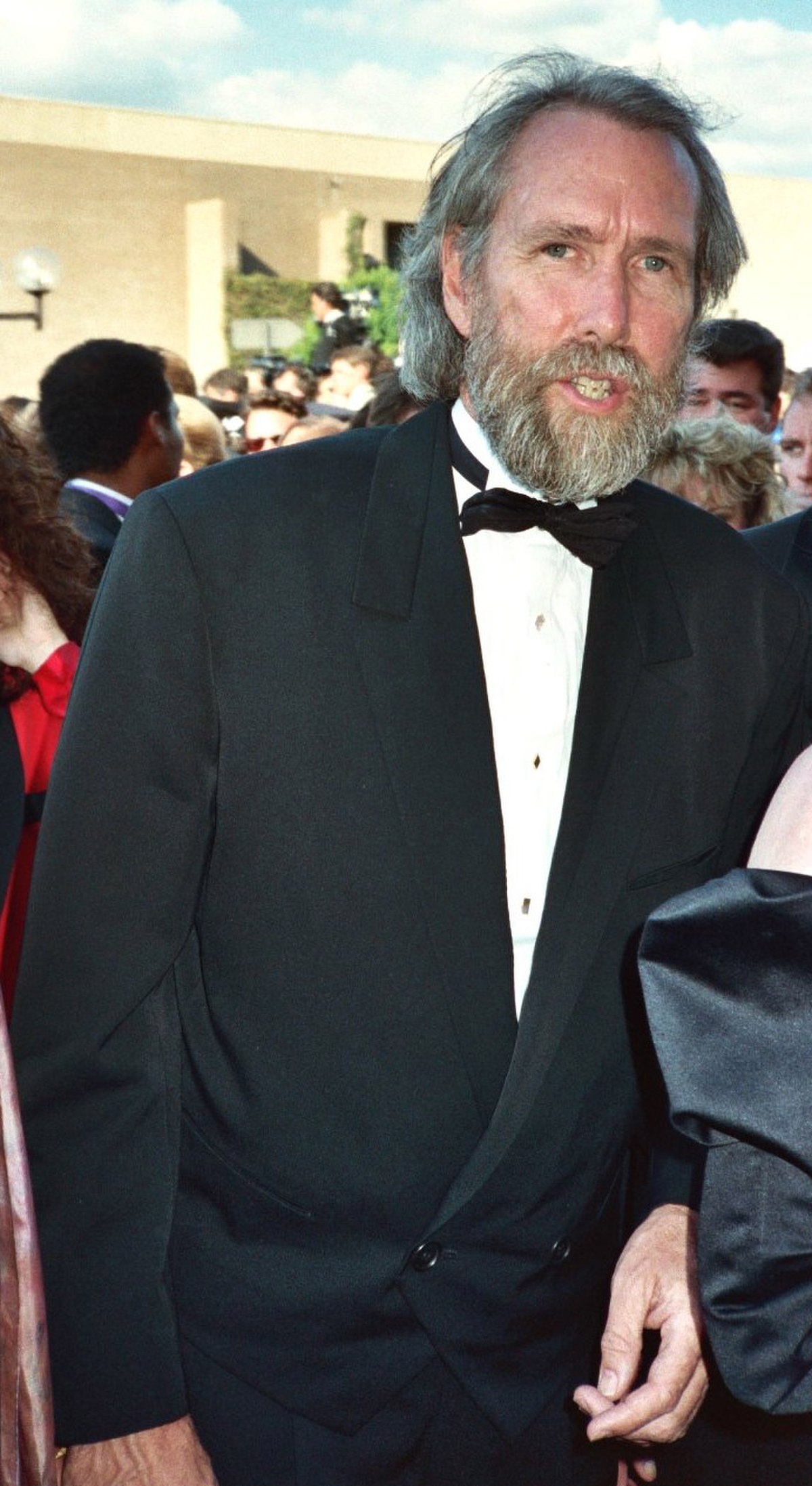 A tall， thin man in his early fifties， with salty-gray hair and a full beard， and wearing a tuxedo.