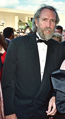 A tall, thin man in his early fifties, with salty-gray hair and a full beard, and wearing a tuxedo.