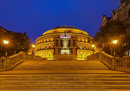 View of the Royal Albert Hall during the blue hour from Prince Consort Road, South Kensington, London (England), showing the South Steps and the statue of Prince Consort Albert (work of Joseph Durham in 1858), to whom the hall was honored by his wife, Queen Victoria. It has a capacity of up to 5,272 seats, and since its opening by Queen Victoria in 1871, world's leading artists from several performance genres have performed there. Each year it hosts more than 350 events including The Proms concerts, that take place annually each summer since 1941.