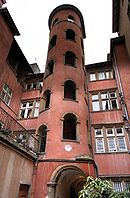 Fotografia a colori di un edificio rinascimentale, con facciata intonacata di rosso, comprendente in primo piano una torre all'interno della quale si eleva una scala a chiocciola.