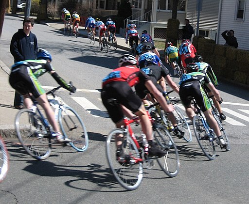 Cyclist are speeding thru a left hand turn at the Tufts Criterium.