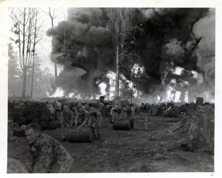 Marine move gas and oil drums away from fire caused by a direct hit by Japanese bombers on a gas and oil dump on Bougainville.