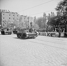 Los hombres de la 51.a División de Infantería (Highland), montados en Universal Carriers, pasan frente a un podio de oficiales superiores durante un desfile de la victoria.