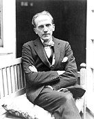 A.A. Milne sitting with arms folded across chest