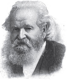 Een man met lang grijs haar, een snor en een lange grijze baard in een zwart jasje en een wit overhemd