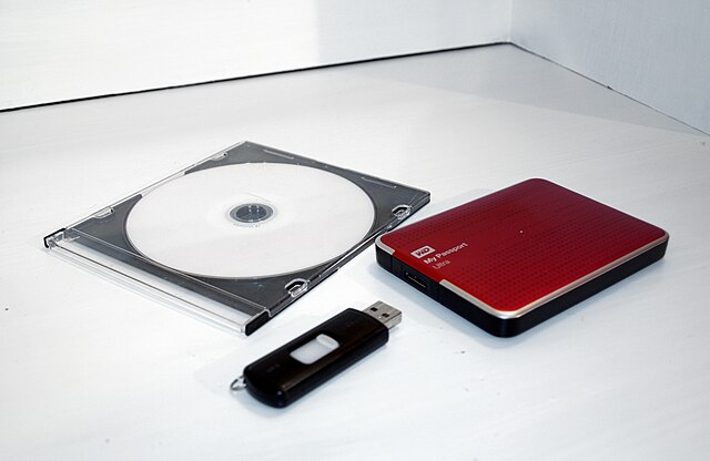From left to right, a DVD disc in plastic cover, a USB flash drive and an external hard drive