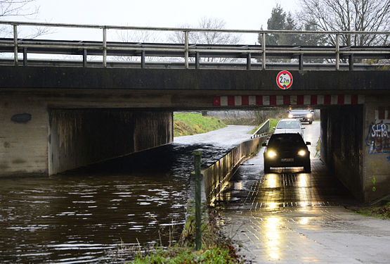 Die Ekholter Au und der Ramskamper Weg beim unwetterartigen Strakregen am 23. Dezember 2014. Die Au ist gerade im Begriff die Straße zu überfluten. Einige Autos durchfahren in letzer Minute die Unterführung.