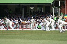 Wicket-keeper in characteristic partial squatting position (together with slip fielders), facing a delivery from a fast bowler. Gilly and the slips.jpg
