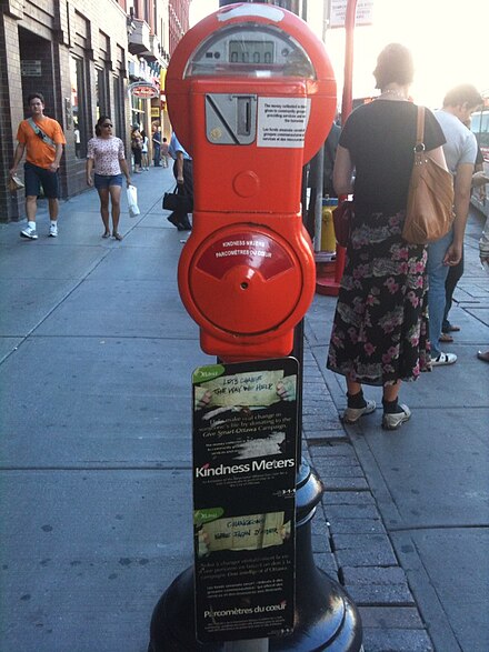 A kindness meter (below the red parking meter) in Ottawa, Ontario, Canada. The meter accepts donations for charitable efforts as part of an official effort to discourage panhandling.