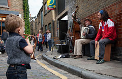 A boy with a toy trumpet in front of a street band. Columbia Market, London, UK