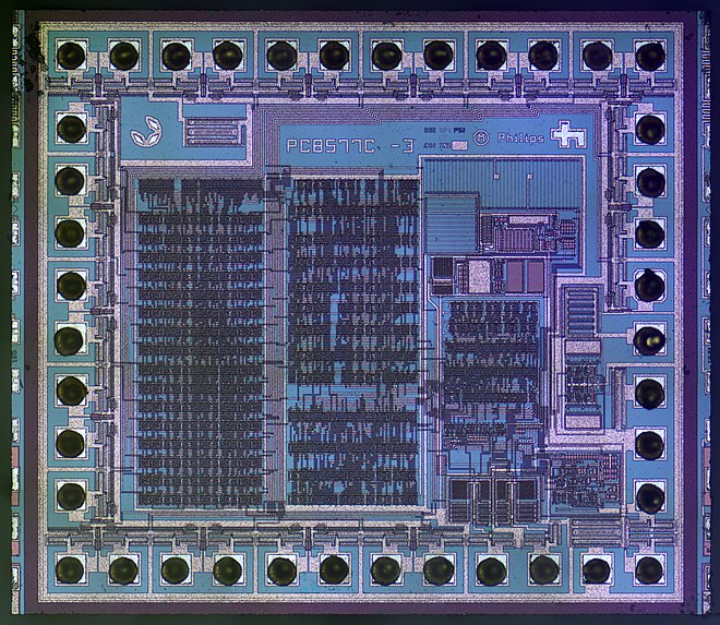 A microscope image of an integrated circuit die used to control LCDs. The pinouts are the black circles surrounding the integrated circuit.