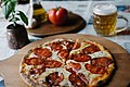 Pizza served on a wooden plate with beer and tomator in the background (49409654698).jpg