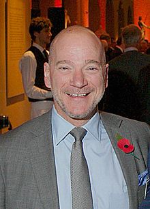 close-up of Andrew McAfee wearing a gray suit and tie, with a light blue shirt underneath, grinning at camera
