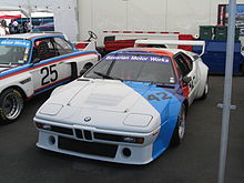 BMW M1 Procar pintado de blanco en su diagonal con los colores de BMW Motorsport exhibido en un stand