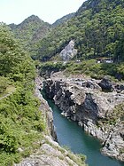 Kleurenfoto van een rivier die een canyon oversteekt tegen de achtergrond van een bos.