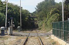 Une entrée de tunnel au loin, la voie ferroviaire qui y mène traverse d'abord un passage à niveau.