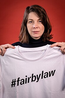 Autorin, Aktivistin und Unternehmerin Lisa Jaspers hält ein Fair-Trade-T-Shirt mit der klaren Aufschrift "#fairbylaw" in die Kamera