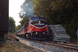 Een diesellocomotief trekt een passagierstrein over een spoorlijn, op weg naar de waarnemer.  De locomotief heeft het logo van P&W op de neus en is genummerd 4006. Een stapel betonnen bielzen ligt naast het spoor.