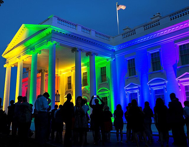 The White House lit with red, orange, yellow, green, blue, and violet lights.