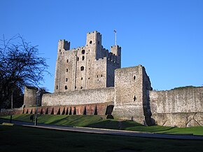 A photograph of a tall stone castle keep; most of the towers are square, but one, rebuilt after a siege, is circular.