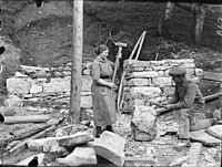 Paul Stang: Žena a muž pracují na řezání kamenů pro opěrnou zeď v pozadí, 1910