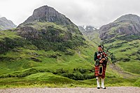 A Scottish Great Highland Bagpipe player, a symbol of Scotland's heritage, playing in front of Bidean nam Bian on the southern side of Glen Coe.