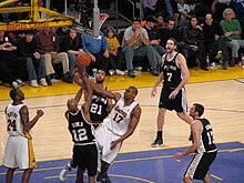 Deux joueurs des Spurs luttent sous le panier avec un joueur des Lakers, sous les yeux de Kobe Bryant et deux Spurs.