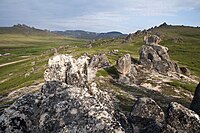 Blick von oben auf einen Hügel eines grasbewachsenen Tals und Felsen im Vordergrund