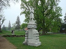 Statue af en soldat, der holder en riffel placeret på jorden ved tønden.