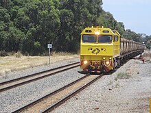 Yellow diesel locomotive hauling brown hopper wagons