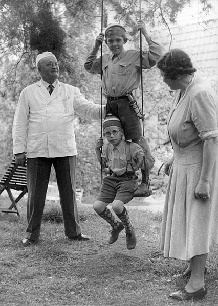 File:Man-and-woman-standing-and-their-children-swinging-in-the-park-142461565996.jpg