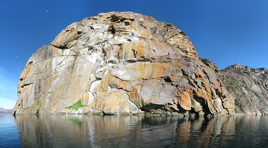 Panorama of the island Nunâ east of Upernavik and south of Aappilattoq in Greenland. Photographed south of the island during a sail trip to Upernavik Icefjord. The mountain, which extends 270 m above sea level, is inhabited with Glacous Gulls (Larus hyperboreus). The white areas are bird droppings. The yellow areas are lichen (probably Caloplaca and Xanthoria) adapted to the nutritious environment. The image has been generated using Hugin based on 17 individual photos arranged in three rows. The images were taken with a hand-held camera (Canon DIGITAL IXUS 800 IS) in a small boat that was slowly drifting (not optimal, but it was too deep to anchor). Vignetting has been minimized using a best fit polynomial in Hugin. The output image from Hugin has been rectangularly cropped in GIMP. The colour value curve has been modified slightly to compensate for over-exposure in certain white areas. Hereafter the photo has been Smart Sharpened with a pixel radius of 3.0 and an amount of 30%. the inverted edge detected mask was used in RGB to apply a selective gaussian blur with pixel radius 5.0 of the sky in an attempt to remove noise there. "Missing sky" in the upper left corner has been pasted in by simple colour picking and painting (do not know other methods).