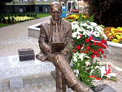 Photographie d'une statue assise sur un banc et regardant un document entre ses mains.