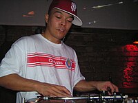 This photo of DJ Qbert shows the standard turntablist technique of manipulating the record with one hand while the other hand adjusts the controls on the DJ mixer. QbertInBerlin.JPG