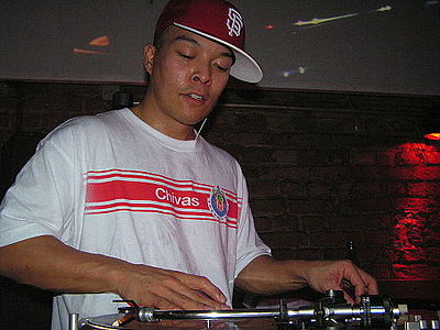 This photo of DJ Q-Bert shows the standard turntablist technique of manipulating the record with one hand while the other hand adjusts the controls on the DJ mixer.