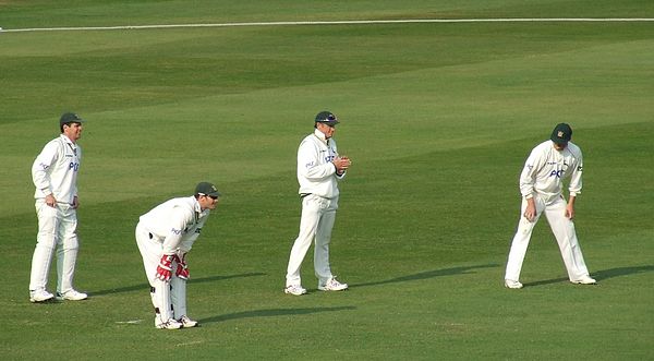 A wicket-keeper (bending down) and three slips wait for the next ball. The batter – out of shot – is a left-hander.