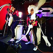 Ripley Clipse demonstrates use of the Streamerator 2000 - a custom-built, motorized toilet paper launcher. It is one of the gadgets used during live shows. The Phenomenauts - Ripley Angel Atom - Streamerator Action Shot - The Slidebar Rock N Roll Kitchen 2017 - Photo by Erica Dominguez.jpg