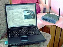 一台黑色笔记本电脑与一台放在后面的无线路由器