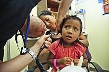 Homme utilisant un otoscope sur une fillette inquiète tenant un ballon