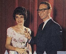 Brian Henderson stands next to Patsy Ann Noble holding a microphone towards her