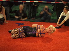 A female rigger stands by while a female model she has tied up tries to free herself BoundCon 2015 escape challenge 1.jpg