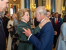 Queen Anne-Marie of the Hellenes (pictured, on the left, at the coronation reception) was the first non-reigning royal to announce her attendance. Buckingham Palace reception (52873211796).jpg