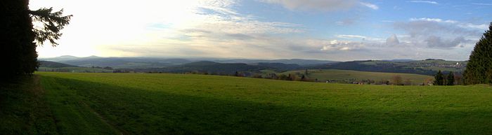 Gesamtblick:
Links der Große (679 m) und der Kleine (641,3 m) Gleichberg im Grabfeld hinter dem Klingeberg (677,2 m); rechts der Mitte der Priemäusel (624,6 m) vor dem Solaberg (577,3 m, links davon) im Buntsandstein-Vorland; rechts der Bildmitte im Hintergrund das Gewerbegebiet Suhl-Friedberg und der Kleine Thüringer Wald mit Schneeberg (692,4 m) und Schleusinger Berg (663,2 m). Nach rechts folgt der Kohlberg (730,3 m), der weiter rechts in den Simmersberg (780,8 m) mit dem Ort Schnett übergeht; dazwischen im Hintergrund der Adlersberg (849,9 m) mit dem Neuhäuser Hügel (890,6 m) im höheren Thüringer Wald, rechts ist im Vordergrund der Ort Waffenrod/Hinterrod erkennbar, der durch das tiefe Bibertal vom Simmersberg getrennt ist.