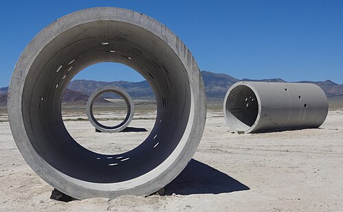 Three large hollow concrete cylinders laying near each other in a desert landscape