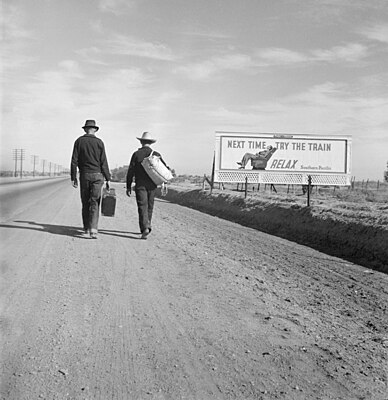 Toward Los Angeles, California, Mars 1937. Two men walking near a billboard that says "Next time, try the train. Relax."